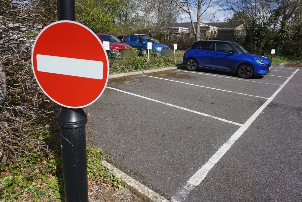No entry sign beside empty marked bays, with parked cars and candidate parking signs behind
