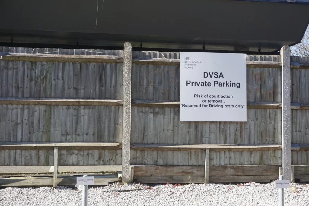 DVSA Private Parking sign on a wooden fence, reserved for driving tests only, above a gravel car park