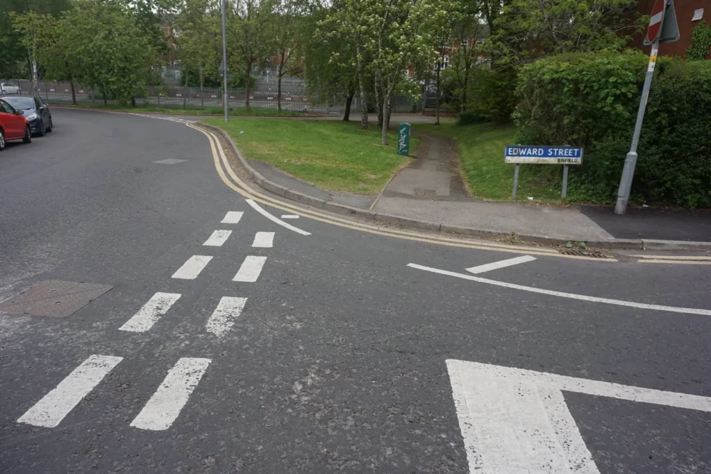 Double broken white give way lines and a painted triangle across the mouth of a quiet side road