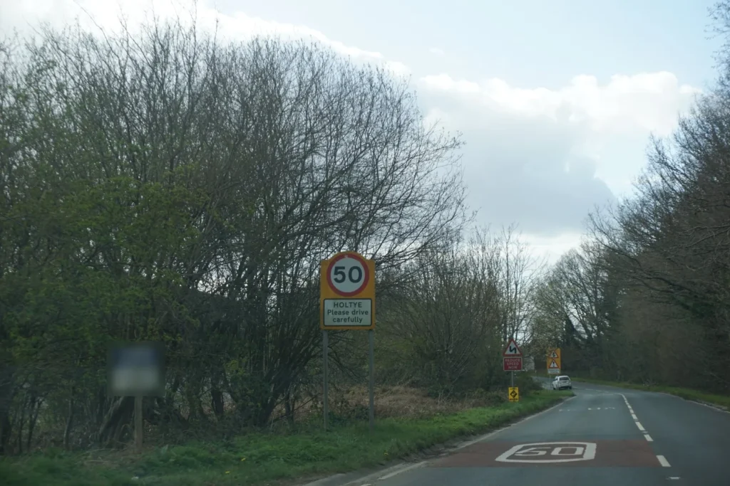 50 mph speed limit sign above a Holtye please drive carefully plate, with 50 painted on red surfacing