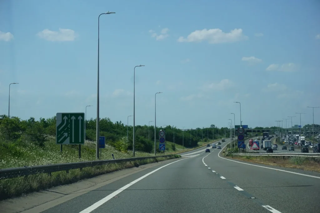 Two lane link road with a green lane merge sign, a 50 limit sign and busy traffic to the right