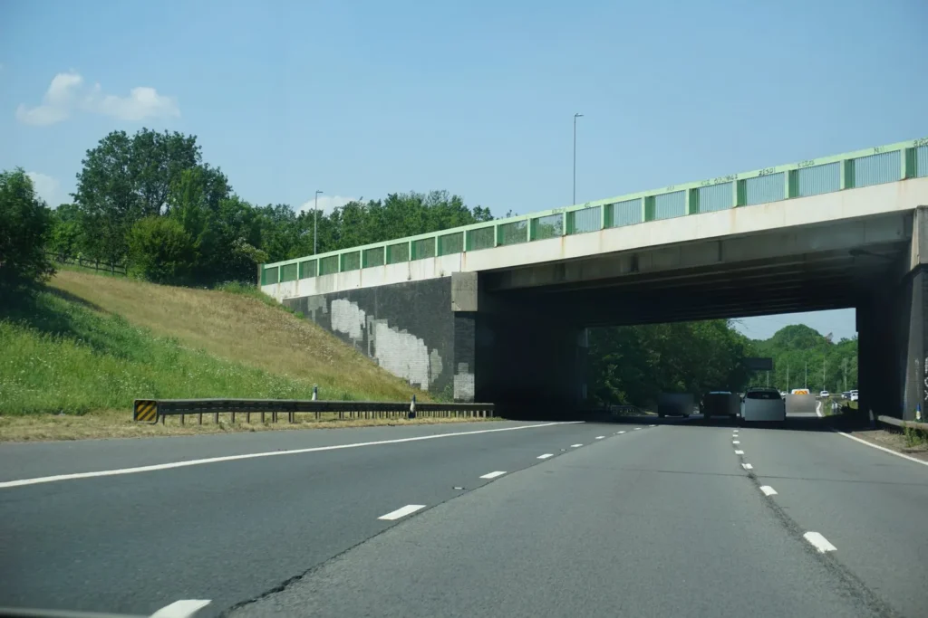 Motorway traffic in three lanes heading towards a concrete overbridge under a blue sky