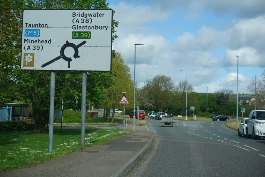 Large roundabout direction sign listing Taunton, Minehead, Bridgwater and Glastonbury, with traffic on the roundabout