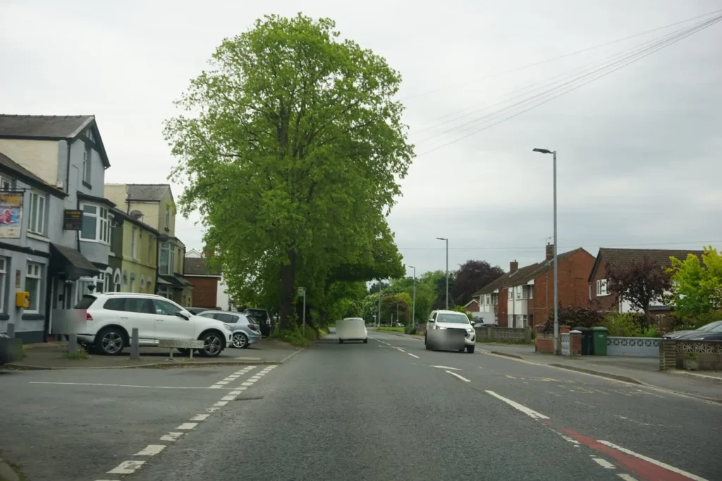 Main road with a side road junction on the left, parked cars by the corner and oncoming traffic