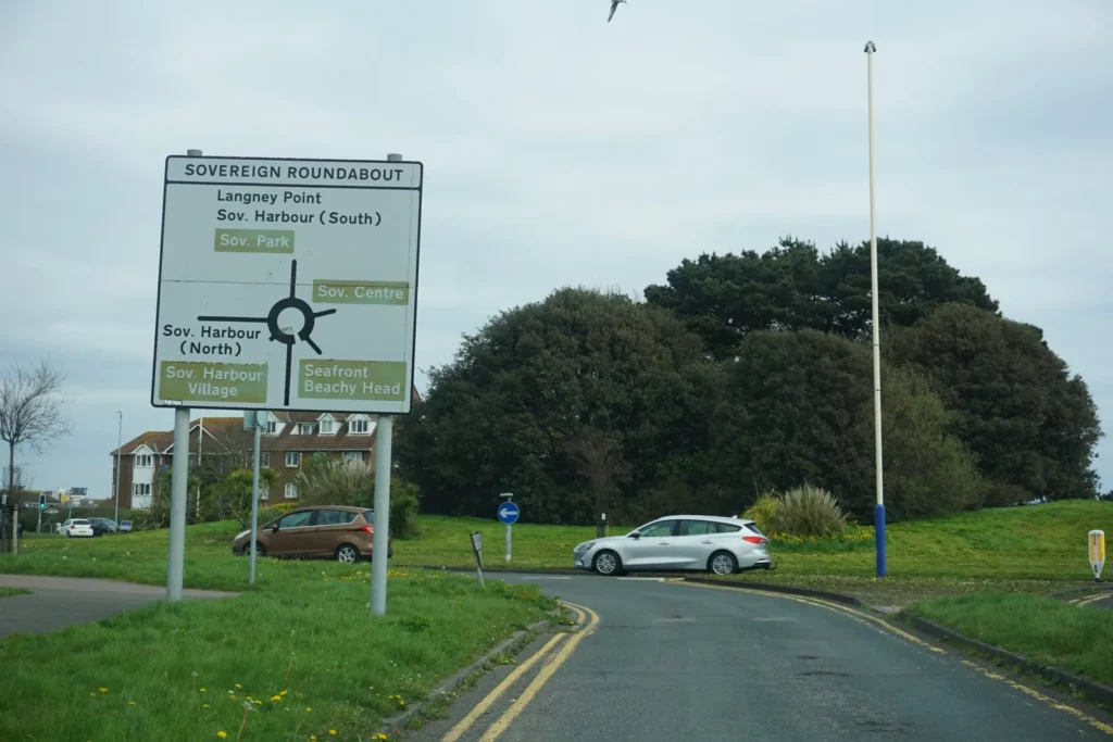 Roundabout map sign for Sovereign Roundabout beside double yellow lines, with traffic circulating behind