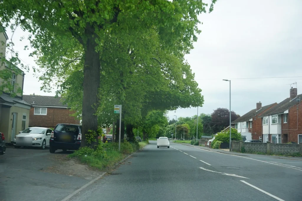 Tree lined suburban road with a bus stop, cars parked by the verge and semi detached houses opposite
